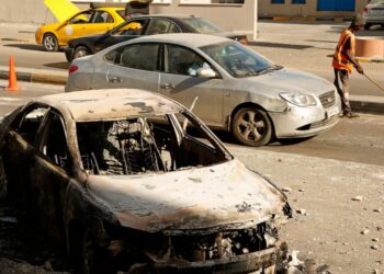A street cleaner sweeps amid the remains of a car that was burned in clashes, in the Libyan capital of Tripoli, Sunday, August 28 2022. Deadly clashes broke out Saturday in Libya's capital between militias backed by its two rival administrations, por