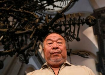 Chinese artist Ai Weiwei poses in front of his unveil glass body of work 'La Commedia Umana' a huge hanging glass sculpture otherwise referred to as a 'chandelier' at the San Giorgio deconsecrated church in Venice, Italy, Friday, Aug. 26, 2022. Chine
