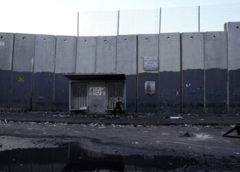A child sits at a bus stop in the besieged Shuafat refugee camp in east Jerusalem, Thursday, Oct. 13, 2022.It was the site of fierce clashes after Israeli security forces set up checkpoints that choked off the only exit and entry points of the camp d