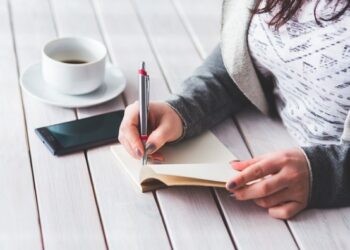 Mujer escribiendo en libreta mientras toma cafe